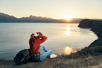 Man sitting by lake against sky during sunset