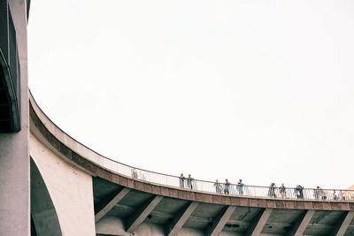 Low angle view of people standing by railing on bridge against clear sky