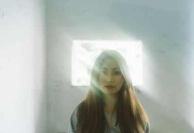 Portrait of young woman standing against window at home