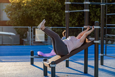 Senior plus size woman doing abdomen exercises working out at municipal sports ground outdoors 