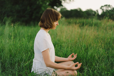 Girl in a white t-shirt doing yoga in a beautiful field. healthy lifestyle and mindfulness concept