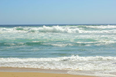 Waves rushing towards shore against clear sky