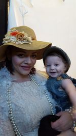 Portrait of smiling woman carrying cute daughter while standing against wall