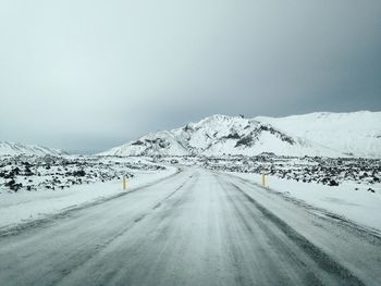 Snow covered road by mountain against sky