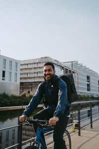 Portrait of smiling young male delivery person cycling on footpath in city