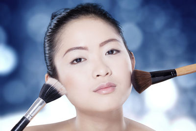 Portrait of young woman with make-up brushes on cheek