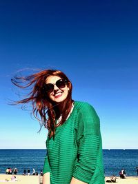 Portrait of young woman wearing sunglasses on beach against clear sky