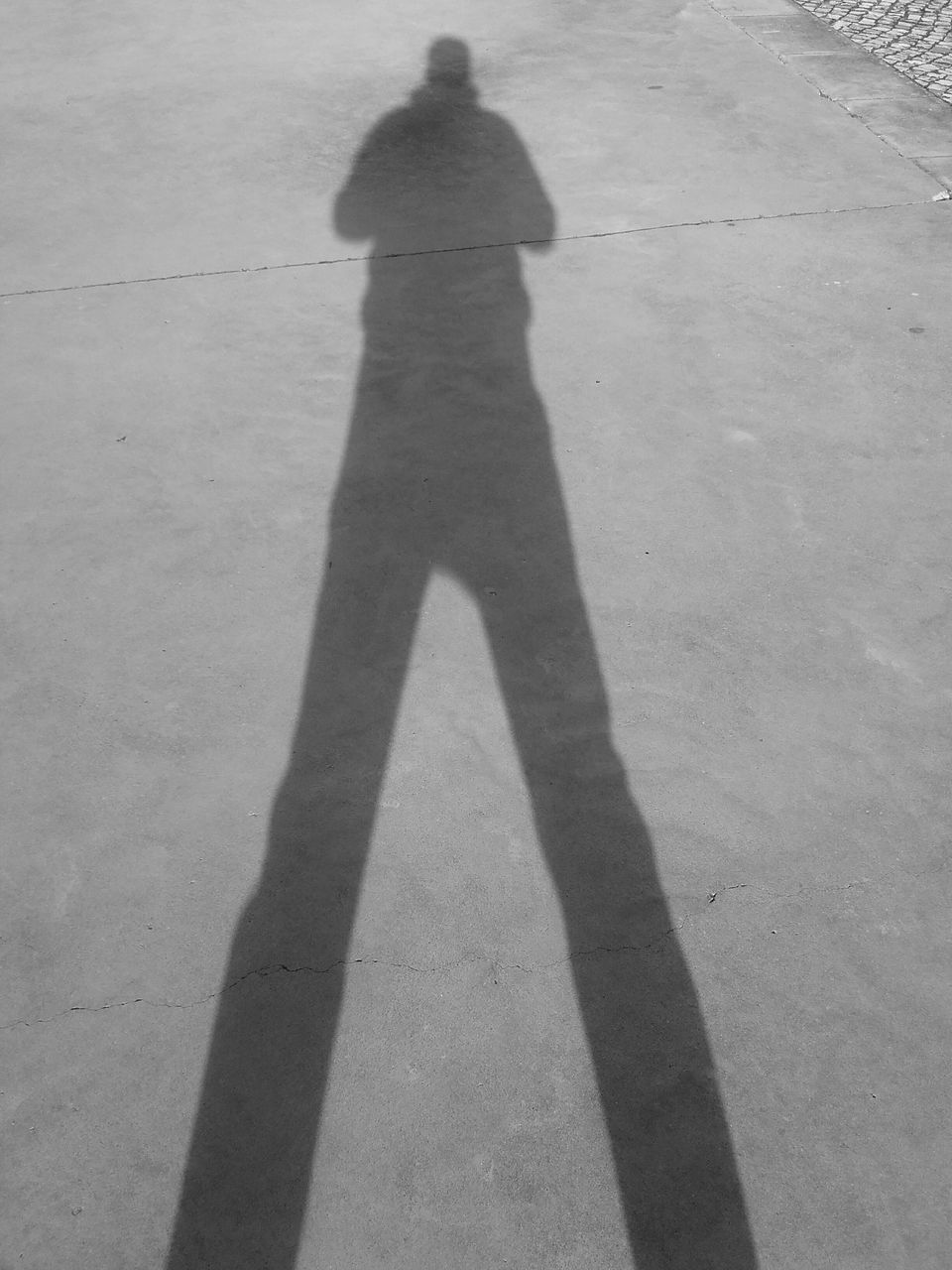 SHADOW OF MAN STANDING ON COBBLESTONE