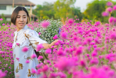 Portrait of beautiful woman standing by pink flowering plants
