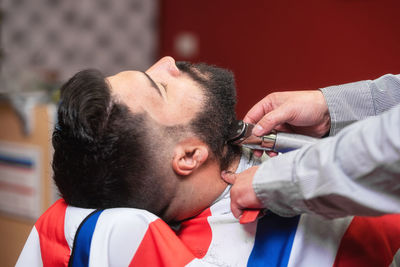 Cropped hands of barber shaving male customer beard in salon