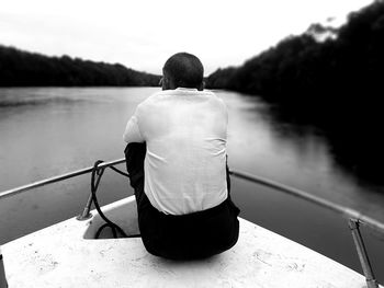 Rear view of man sitting on long tail boat at lake