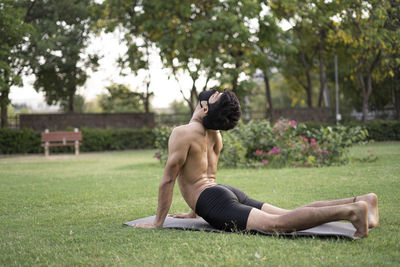 Side view of shirtless young man sitting on grass