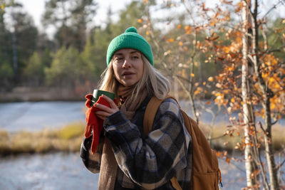 Female tourist resting after hiking, drinking hot tea, listening to sounds, noise in pine forest