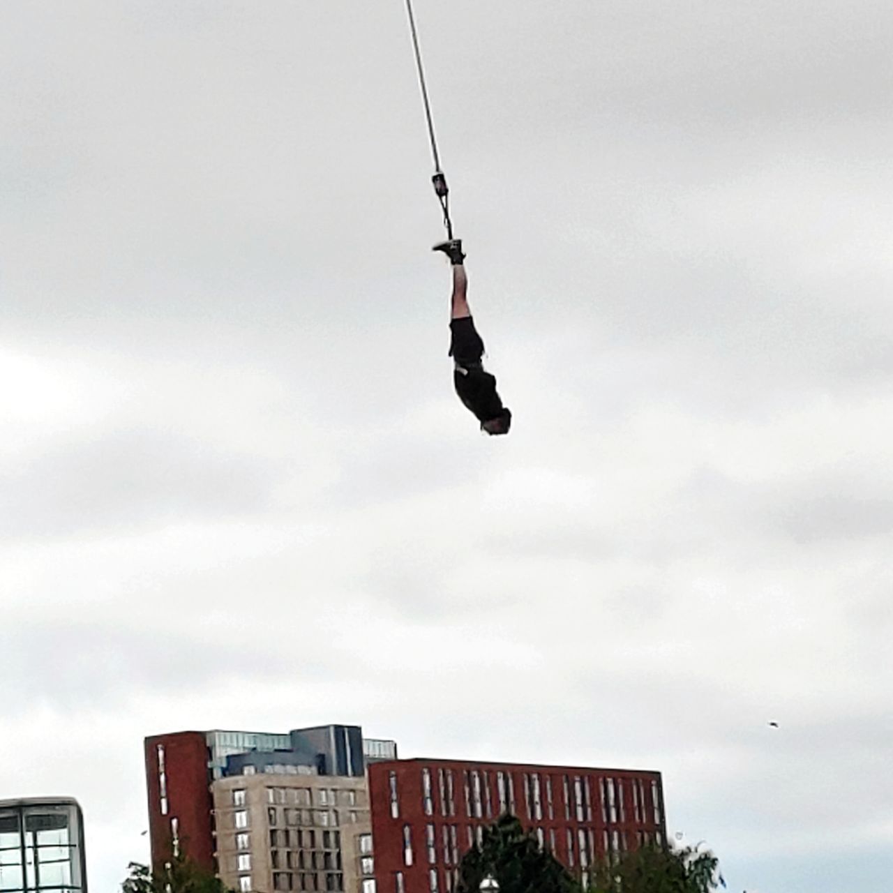 LOW ANGLE VIEW OF MAN FLYING HANGING AGAINST BUILDING