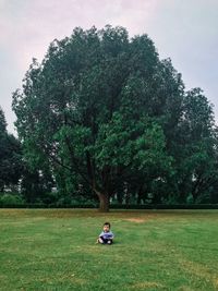 Man sitting on field against trees