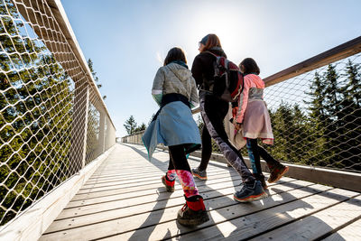 Rear view of people on footbridge against sky