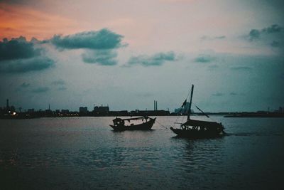 Boats sailing in sea at sunset