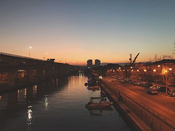 Silhouette bridge over river in city against sky during sunset