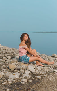 Young woman sitting on beach against clear sky