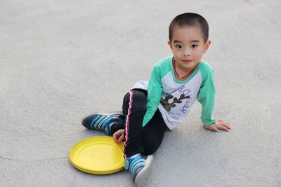 Portrait of boy sitting with plastic disc on footpath at park