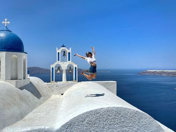 Rear view of woman standing by sea against clear blue sky