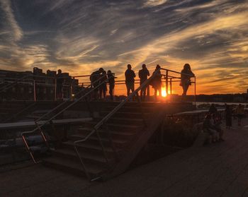 Silhouette people on railing at sunset