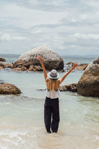 Woman with arms raised standing in sea against sky