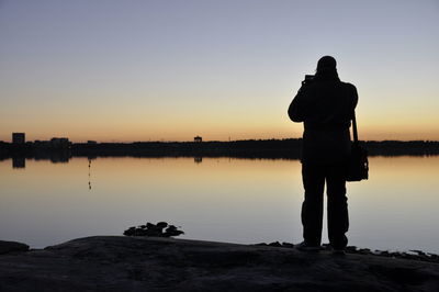 Rear view of silhouette man standing by lake against sky during sunset