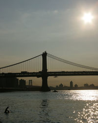 Silhouette of suspension bridge over river during sunset