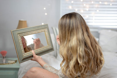 Woman applying make-up in front of mirror at home
