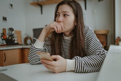 Young woman using mobile phone while sitting at home