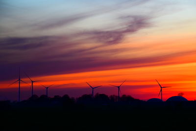 Silhouette windmills on field against sky during sunset