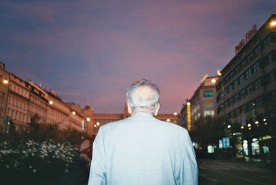 Rear view of man on city street against sky at night