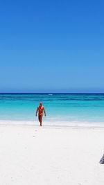 Full length of man walking at beach against clear blue sky during sunny day