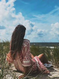 Rear view of woman sitting on rock against sky