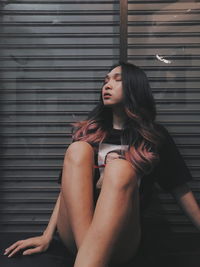 Side view of young woman sitting against wall