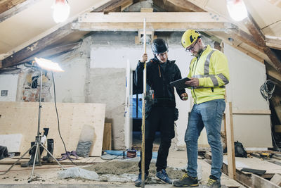 Full length of male construction workers discussing over digital tablet while working at site