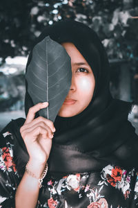 Portrait of woman holding leaf over face