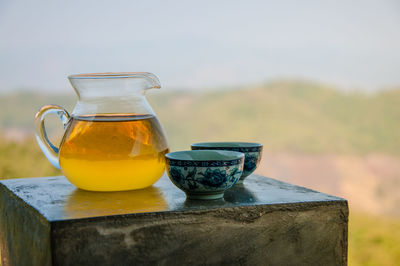 Tea in jug with cups on table against mountain