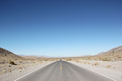 Empty road in desert against clear blue sky