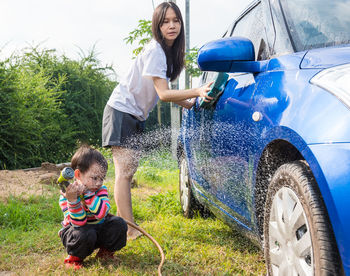 Full length of mother and son cleaning car outdoors