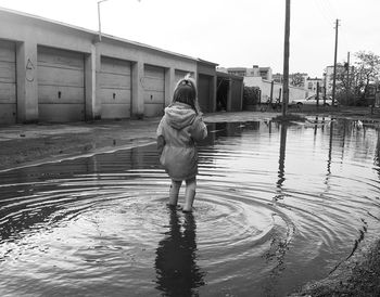 Rear view of girl standing in puddle against sky