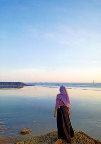 Rear view of woman sitting on beach against sky