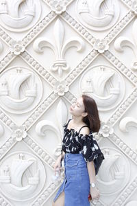 Woman looking away while standing against white wall