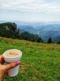 Midsection of person holding cup by mountain against sky