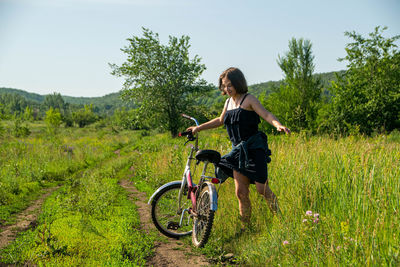 Girl standing with bicycle at field against sky