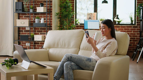 Young woman using phone while sitting on sofa at home