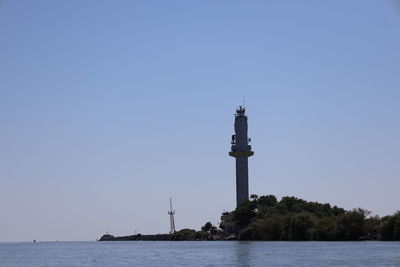 Lighthouse by sea against clear sky