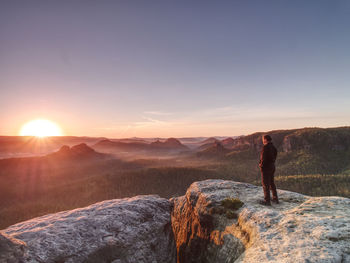 Hiker watch sunrise in rocky misty landscape. travel alone. man standing on mountain summit