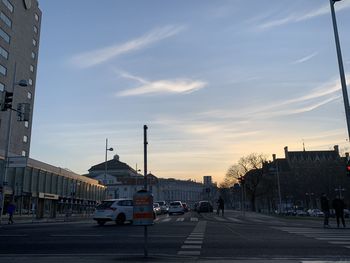 City street by buildings against sky during sunset
